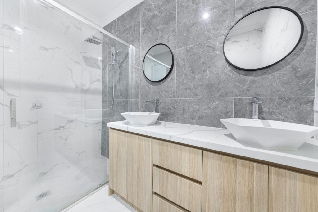 Stylish and elegant modern bathroom featuring double sinks, oval mirrors, and marble tiles.